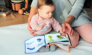 Maluch z zaciekawieniem ogląda książeczkę, ucząc się od kiedy czytać dziecku. Obok instrumenty muzyczne.