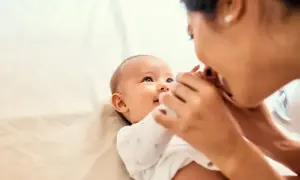 Uśmiechnięte dziecko reaguje na imię, gdy mama pochyla się, by je pocałować.