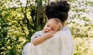 Ciepły uścisk mamy, kiedy dziecko zaczyna się przytulać. Maluch wtulony w ramię, otoczony zielenią.