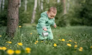 Dziecko w zielonym kombinezonie, z konewką w ręku, odkrywa świat wśród traw i mleczy. To jego **3 skok rozwojowy**, pełen ciekawości i nowych doświadczeń.