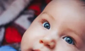 Niebieskie oczy noworodka otwierają się na świat. Widać zaciekawienie i zdumienie w jego spojrzeniu.