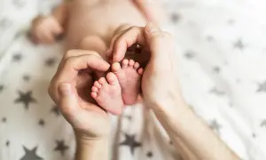 Dłonie otaczają maleńkie stópki 7 tygodniowego dziecka. Delikatne paluszki i pięty są objęte czułością.