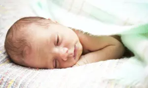 Śpiące niemowlę z lekko wydłużoną głową ułożoną na kolorowym kocyku, otulone miętowym kocykiem.