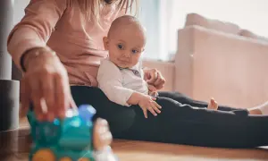 Mama bawi się z 9-miesięcznym dzieckiem, które siedzi na jej kolanach. Przed nimi leży zabawkowy pociąg.