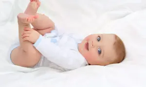 Uśmiechnięte niemowlę na białym tle, odkrywające swoje nóżki. To uroczy obrazek pokazujący rozwój dziecka miesiąc po miesiącu.