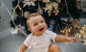 Uśmiechnięte dziecko bawi się światełkami choinkowymi. To magiczny moment, kiedy dziecko zaczyna mówić i odkrywać świat.