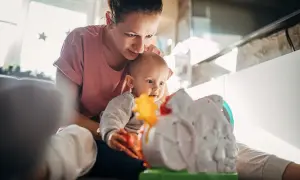 Mama bawi się z 5-miesięcznym dzieckiem, które z zaciekawieniem ogląda kolorową zabawkę.