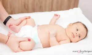Delikatne ćwiczenia bioderek niemowlaka, by zapobiec dysplazji stawu biodrowego. Fizjoterapeuta delikatnie porusza nóżkami dziecka.