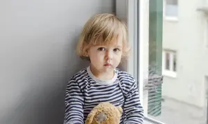 Smutny dwulatek nie mówi, tuli misia przy oknie.