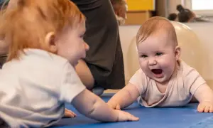 Dwa niemowlęta ćwiczą, by zmniejszyć wzmożone napięcie obręczy barkowej. Jedno z nich śmieje się radośnie.