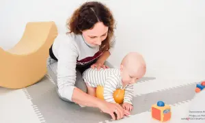 Mama wspiera roczne dziecko w nauce raczkowania. Radosne zabawy z maluszkiem na macie.