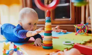Zaintrygowany 6 miesięczne dziecko sięga do kolorowej wieży z kółek, otoczony zabawkami na macie.