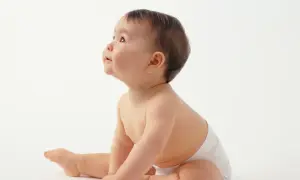Urocze dziecko w pieluszce, które właśnie siada, z zaciekawieniem spogląda w górę.