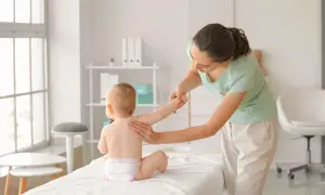 Fizjoterapeutka pomaga dziecku w nauce pełzania do tyłu, delikatnie podtrzymując jego rączki.