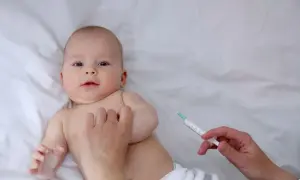 Małe dziecko leży na białym tle, a ręka pielęgniarki przygotowuje szczepienia noworodka w szpitalu.