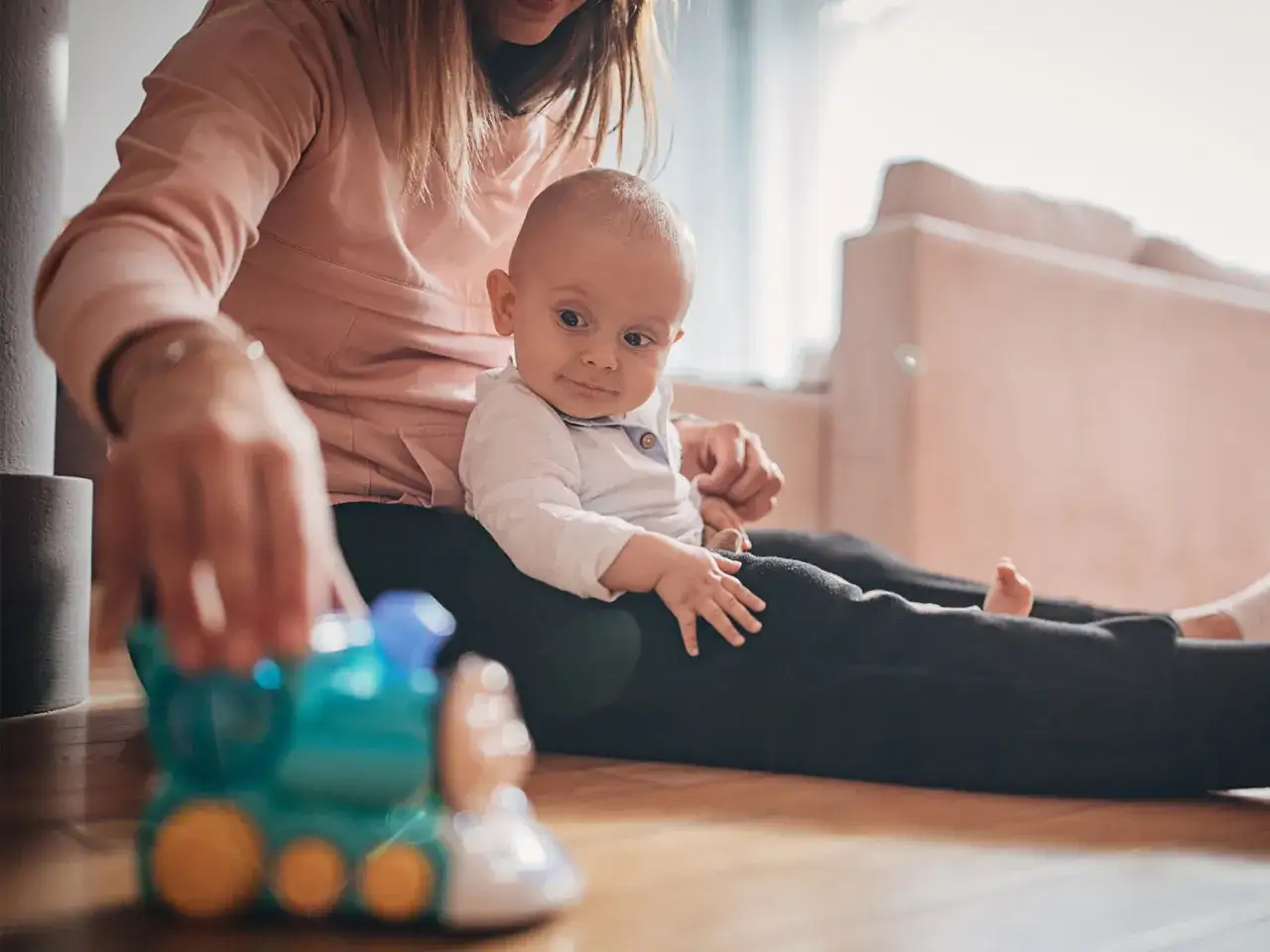 Mama bawi się z 9-miesięcznym dzieckiem, podając mu kolorową zabawkę-pociąg.