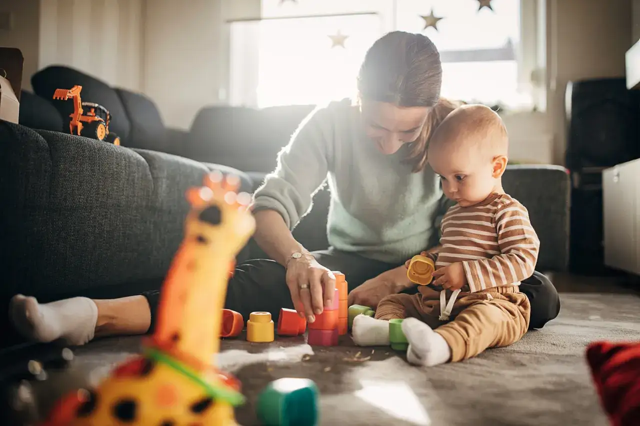 Mama buduje wieżę z klocków z 7 miesięcznym dzieckiem. Maluch z zaciekawieniem obserwuje zabawki.