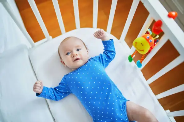 Maluch w niebieskim bodziaku w kropki, leżący w łóżeczku, przeżywa skok rozwojowy 10 tydzień. Z radością podnosi rączki.