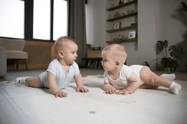 Dwa niemowlaki na macie, każde w body, patrzą na siebie. To ich pierwszy **5 skok rozwojowy**!